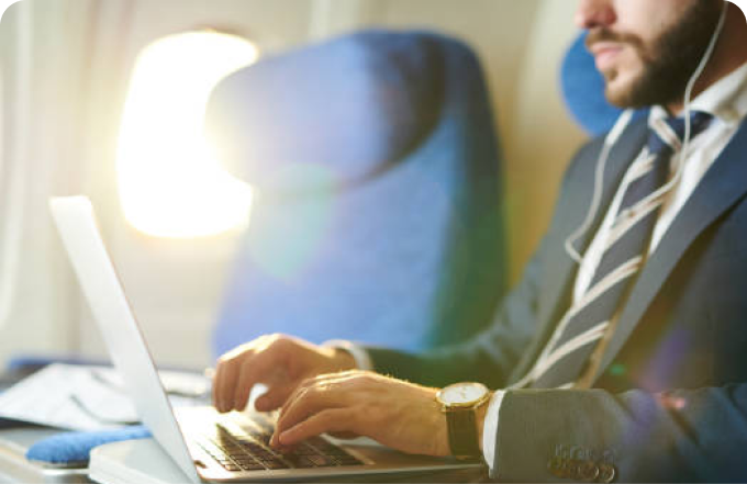 A man dressed in a suit and tie uses his laptop while sitting comfortably on an airplane.
